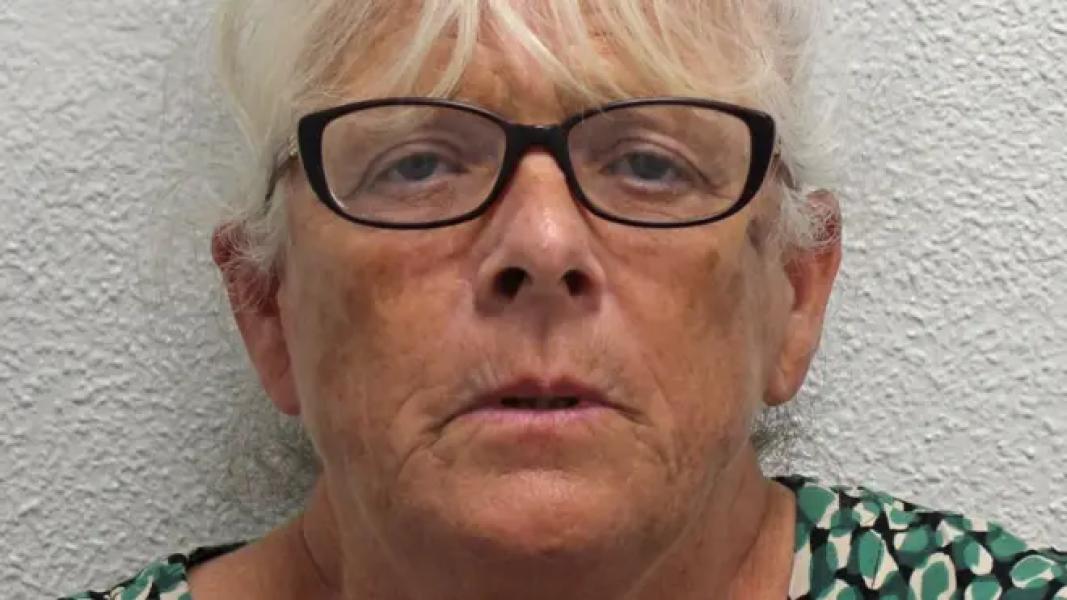 Deborah Mason, a woman with white hair and wearing dark rimmed glasses. She is standing against a white background and wearing a green, white and black patterned top