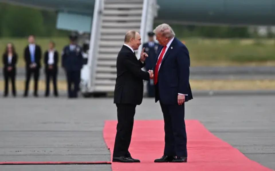 Путін і Трамп стискають руки на червоній доріжці біля трапу літака. Обидва посміхаються, Путін підняв вказівний палець, Трамп ласкаво схилив до нього голову