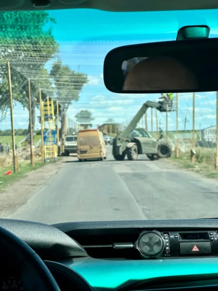 Фото з авто: вздовж дороги що 1-2 метри стоять деревʼяні стовпи, на які зверху та по боках натягнута сітка. Біля одного зі стовпів, на невеликому підйомнику, пофарбованому в оливу, стоять двоє чоловіків. На протилежній стороні стоїть синьо-жовта драбина