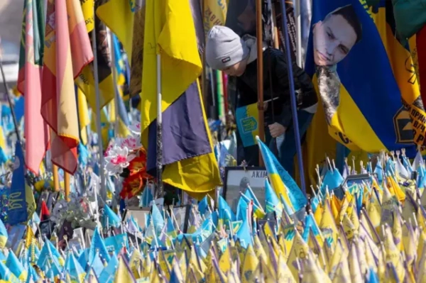 Хлопчик років 5-6 у шапці дивиться на жовто-блакитні прапорці, встановлені у пам&#x27;ять про загиблих 