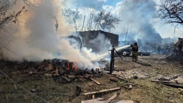 Горять руїни будинку після влучення снаряда, йде сильний дим. Пожежник у споряджені направляє воду на пожежу 