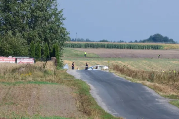 Поліцейська автівка посеред поля, огороджена стрічкою. У полі, на тлі густої кукурудзи, видно людей у зелених жилетах
