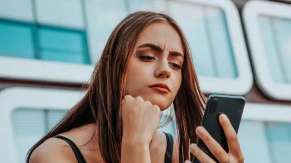 Молода жінка з тривожним виразом обличчя дивиться на свій смартфон