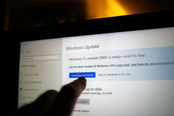 Палець, що вказує на екран Windows Update на ноутбуці, виділяє кнопку «Завантажити та встановити» для Windows 11
