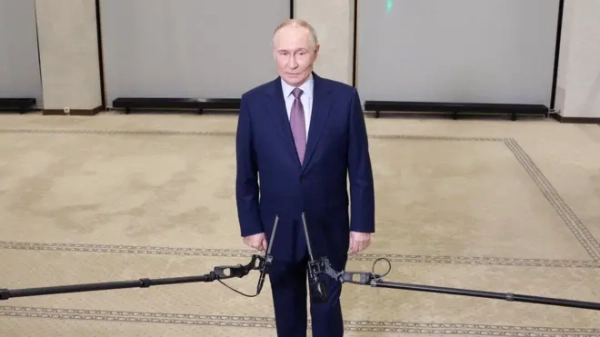 Путін у синьому діловому костюмі стоїть у кімнаті, перед ним тримають мікрофони 