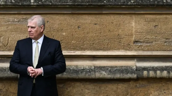 Prince Andrew stands with his back against a stone wall