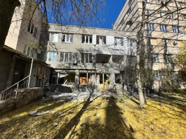 Пошкоджений обстрілами сірий будинок з вибитими вікнами