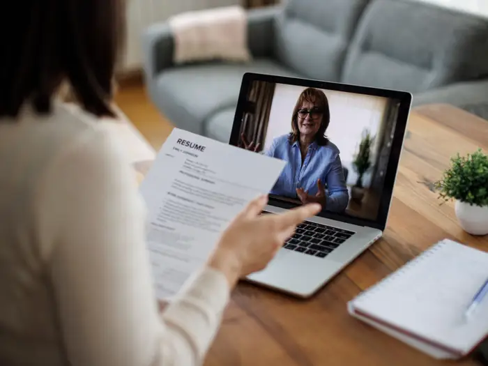 6 помилок у нетворкінгу, які можуть коштувати вам роботи 2 A person holds a resume during a video interview on a laptop at a wooden table.