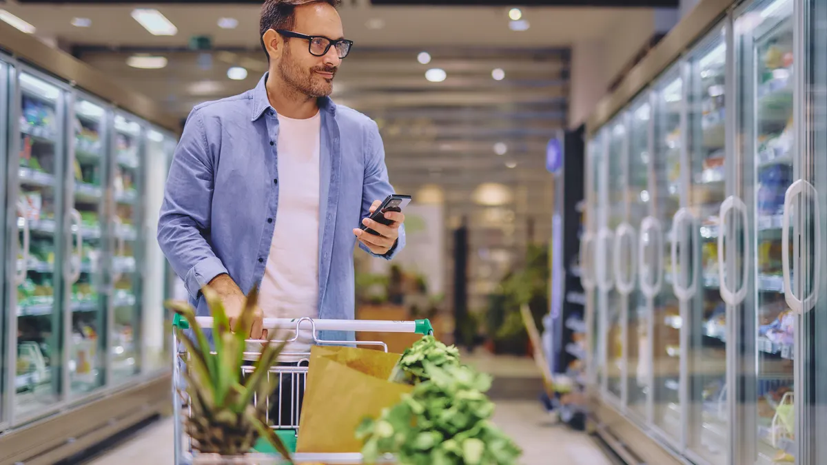Instacart і Shipt впроваджують помічників для покупок на основі ШІ 2 Чоловік перевіряє телефон під час покупок у супермаркеті.