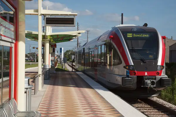 Поїзд Austin MetroRail зупинився на станції легкорейкового транспорту в Остіні, штат Техас, на тлі блакитного неба.