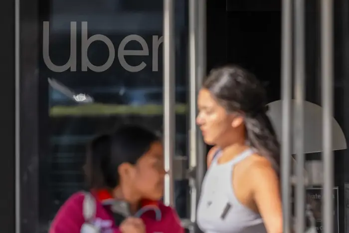 Розмиті пішоходи проходять повз вхід з великим логотипом Uber на скляних дверях.